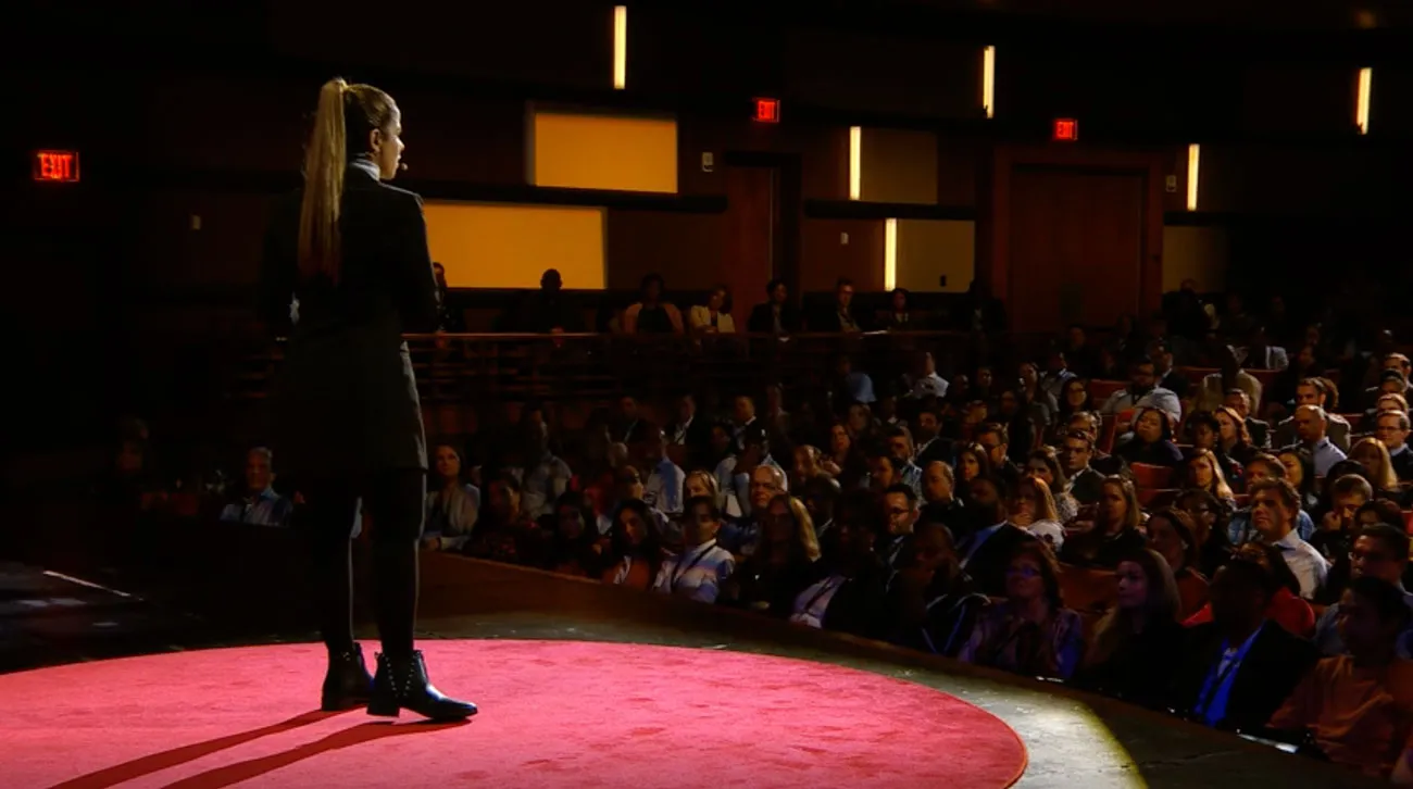 A speaker seen from behind the stage, facing the audience in the house