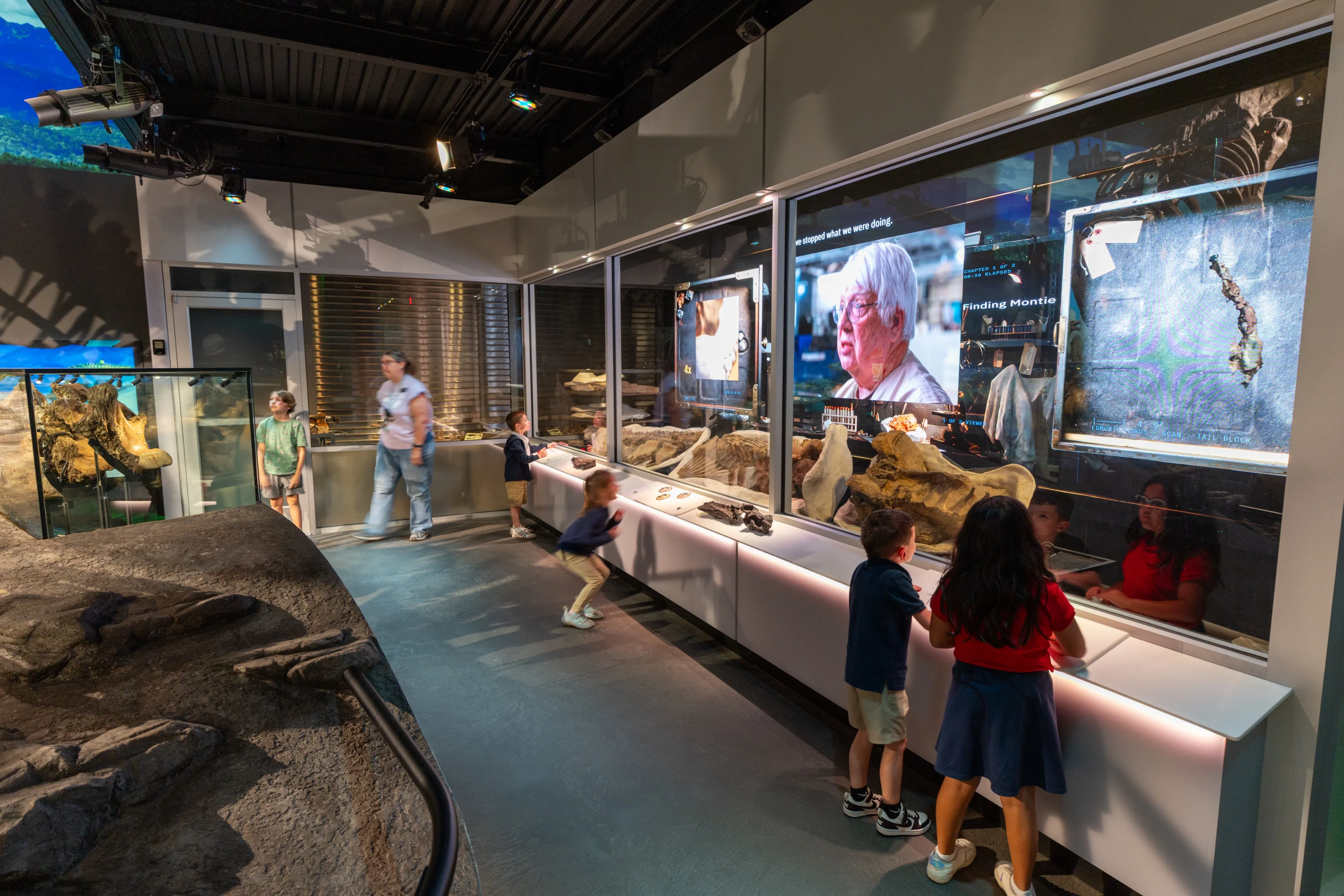 Montie’s Lab: the Edmontosaurus in its working lab setting, visitors at the LED wall behind it
