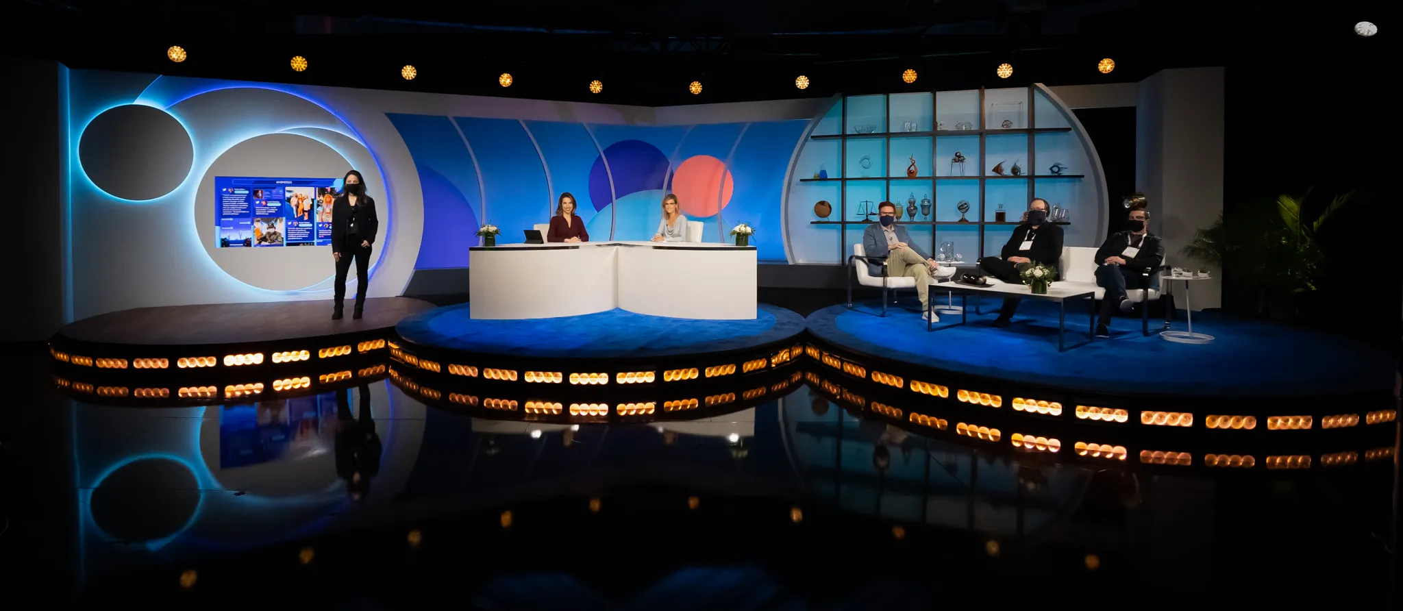 The three-part broadcast studio in blue and white: a standing position, the news desk, and the interview area