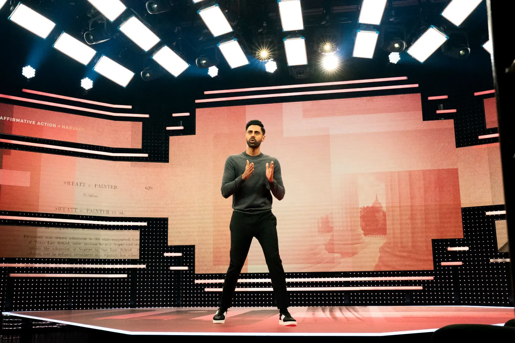 Hasan Minhaj on the Patriot Act stage, LED walls and floor glowing red around him