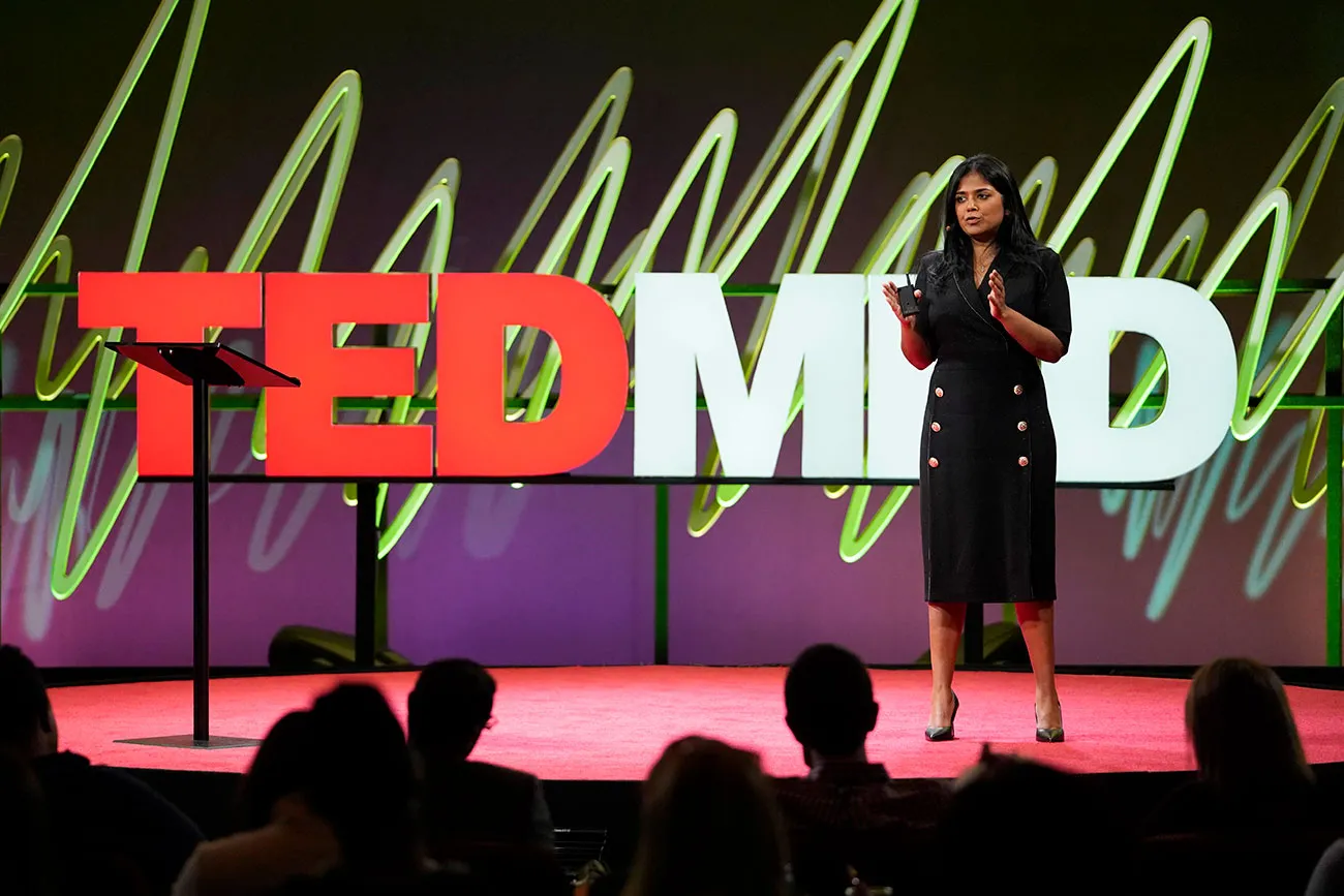 A speaker on the TEDMED stage, a green line pattern across the backdrop behind the red letters